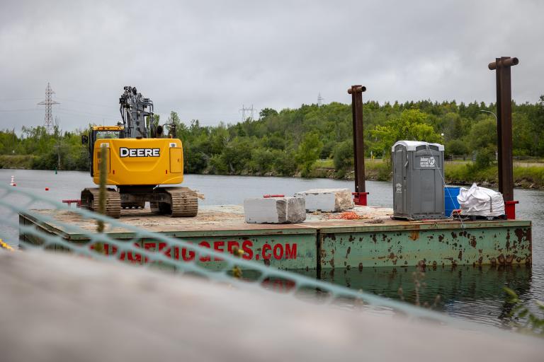 Riverbank reconstruction Barge on Otonabee River with yellow digger on it.